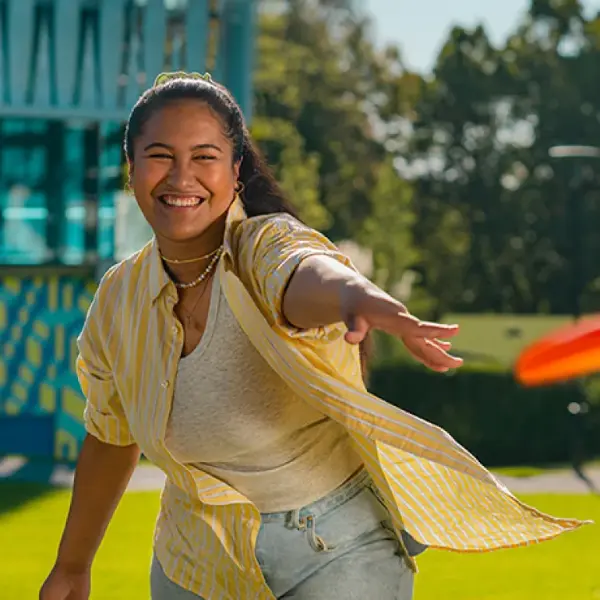 university student in field throwing frisbee on campus